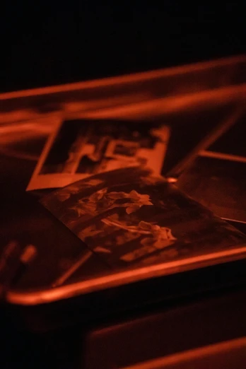 a cell phone sitting on top of a table, inspired by Nan Goldin, holography, collodion photograph, orange glow, closeup photograph, etching