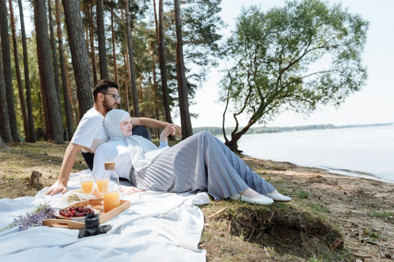 a man and woman sitting next to each other on a blanket, pexels contest winner, hurufiyya, forest picnic, white hijab, at the waterside, breakfast