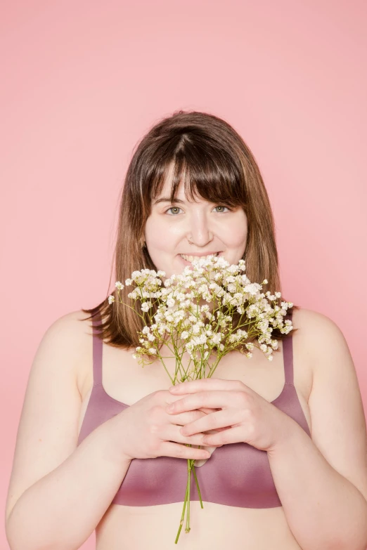 a woman holding a bunch of flowers in front of her face, by Arabella Rankin, brown hair and bangs, solid background, looking happy, plus-sized