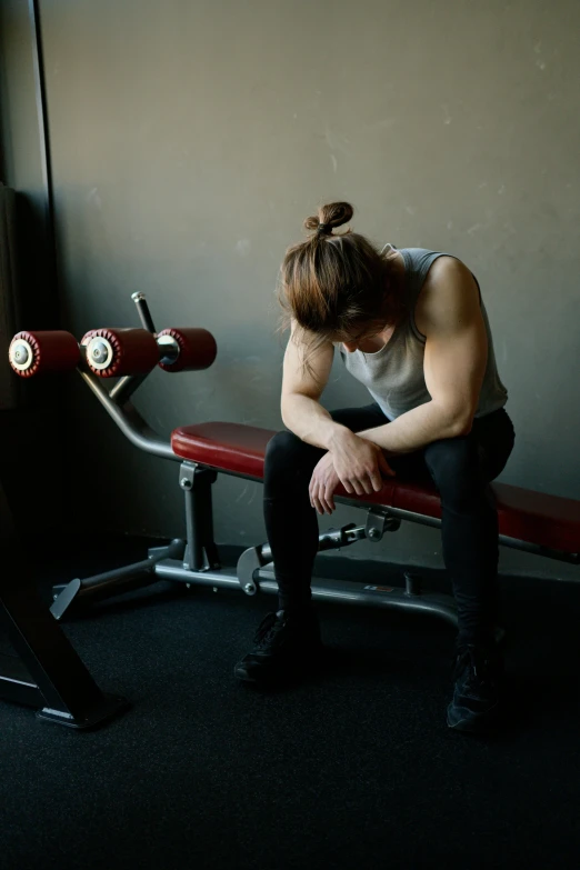 a man sitting on top of a bench next to a window, dim dingy gym, she is distressed, kirsi salonen, disappointed