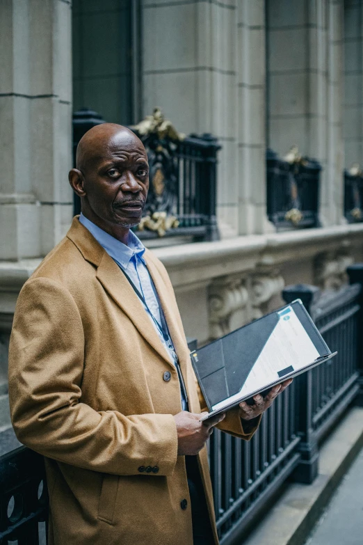 a man standing in front of a building holding a laptop, by Joseph Severn, pexels contest winner, renaissance, lance reddick, holding a clipboard, humans of new york, 15081959 21121991 01012000 4k