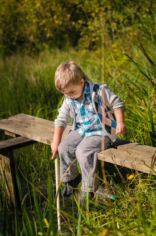 a young boy sitting on top of a wooden bridge, by Julian Allen, holding walking stick, activity play centre, lookbook, near pond