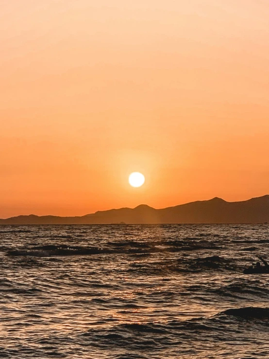 a man riding a surfboard on top of a wave in the ocean, during a sunset, sunset in the distance, greece, ((sunset))