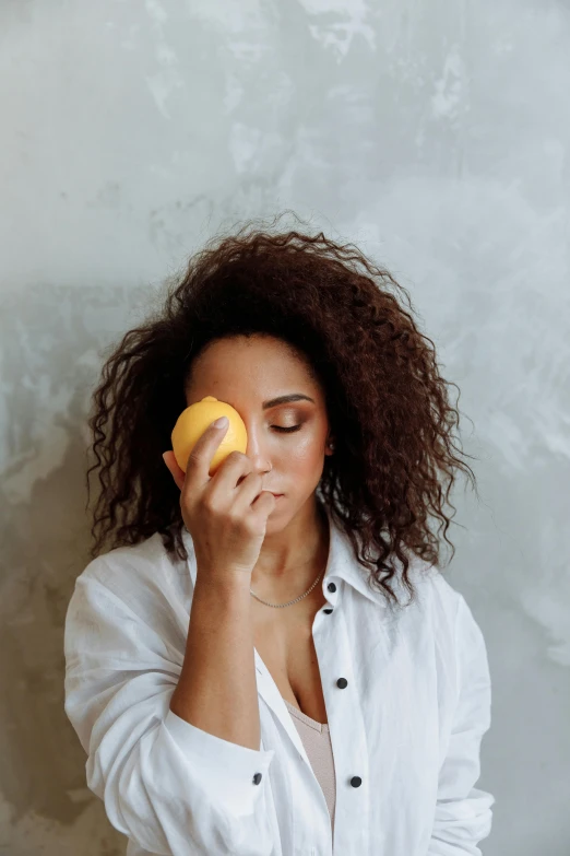 a woman holding an orange in front of her face, trending on pexels, wearing a lemon, putting makeup on, mixed race woman, dry brushing