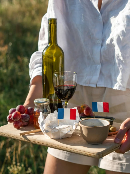 a woman holding a tray with food and wine, inspired by Jules Bastien-Lepage, unsplash, french flag, square, outdoor photo, brown