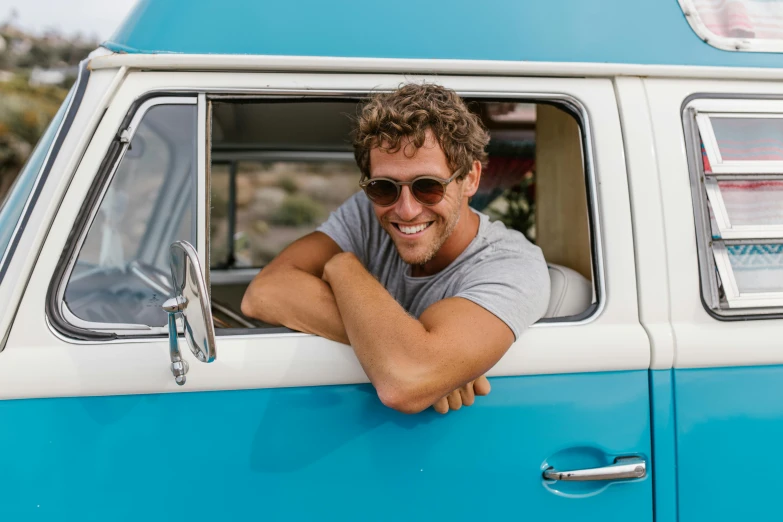 a man sitting in the driver's seat of a blue and white van, pexels contest winner, nate berkus, leaning against the window, kombi, curly haired