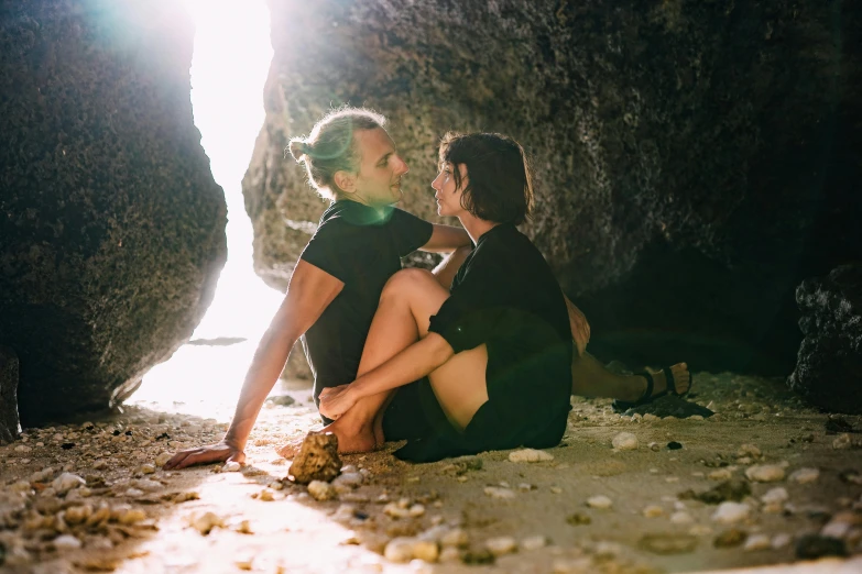 a man and woman sitting next to each other on a beach, unsplash, romanticism, inside of a cave, flirting, abel tasman, lesbians