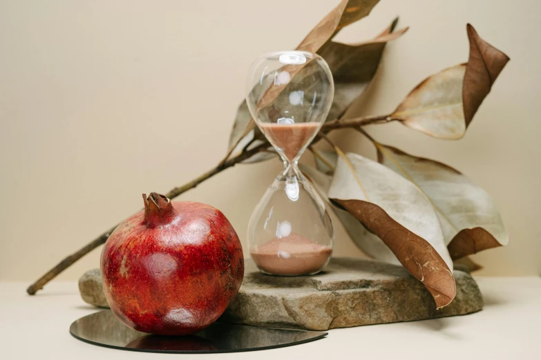 a red apple sitting on top of a table next to a hourglass, a still life, by Julia Pishtar, trending on pexels, pomegranade, next to a plant, humus, high resolution product photo