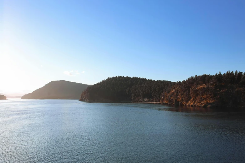 a large body of water surrounded by trees, by Doug Ohlson, pexels contest winner, hurufiyya, picton blue, warm light, sea line, slide show