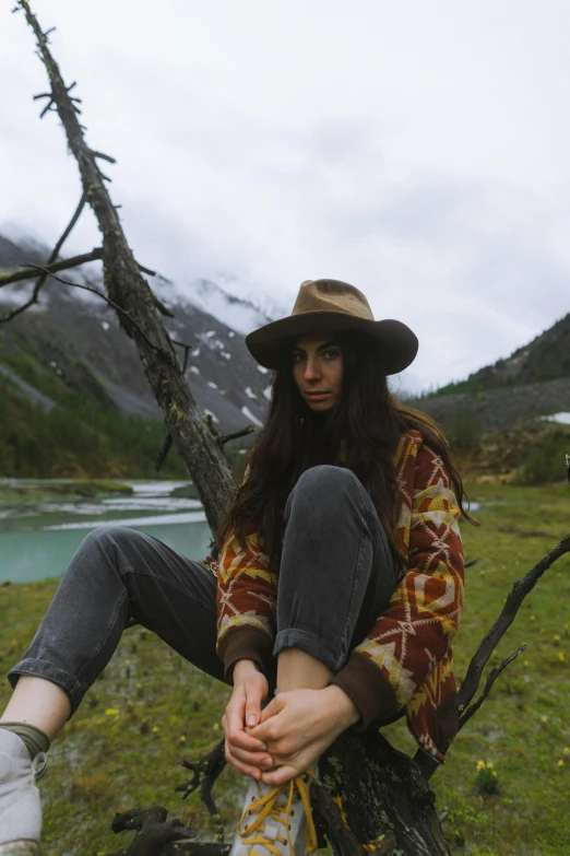 a woman sitting on top of a tree next to a lake, an album cover, pexels contest winner, wearing wool hat, western clothing, julia gorokhova, in mountains