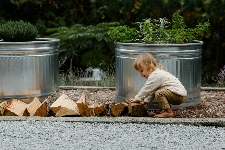 a small child sitting on top of a pile of wood, inspired by Elsa Beskow, unsplash, pots with plants, fire pit, feed troughs, “ iron bark