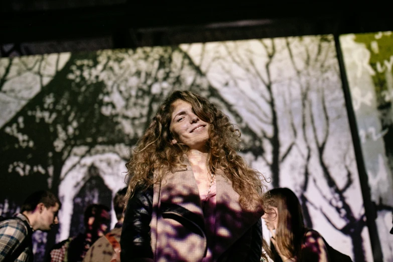 a woman standing in front of a crowd of people, an album cover, by Julia Pishtar, pexels contest winner, happening, with long curly, light smiling, kramskoi 4 k, projection design installation