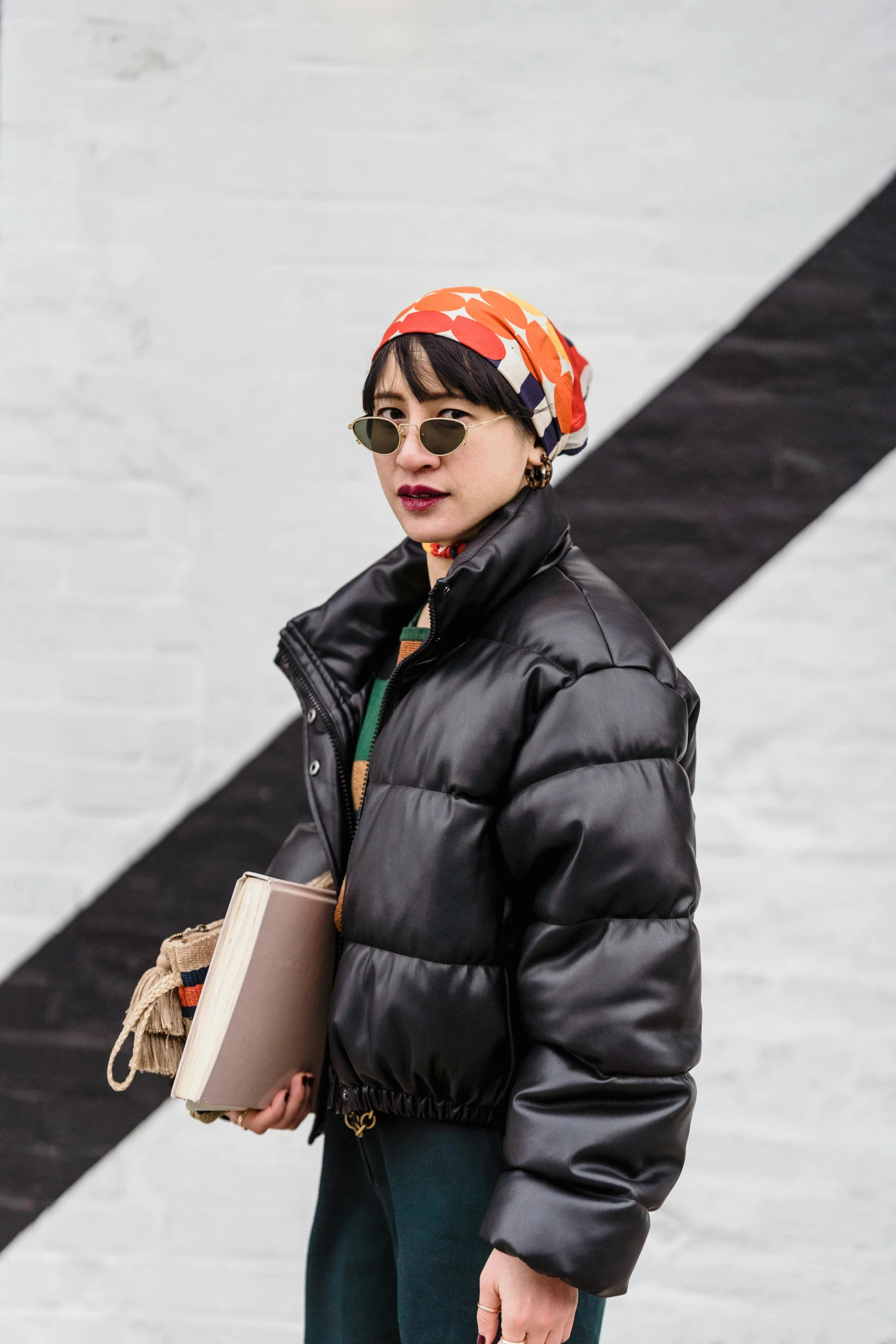 a woman standing in front of a black and white wall, by Nina Hamnett, trending on pexels, pop art, model wears a puffer jacket, wearing a head scarf, at new york fashion week, kiko mizuhara