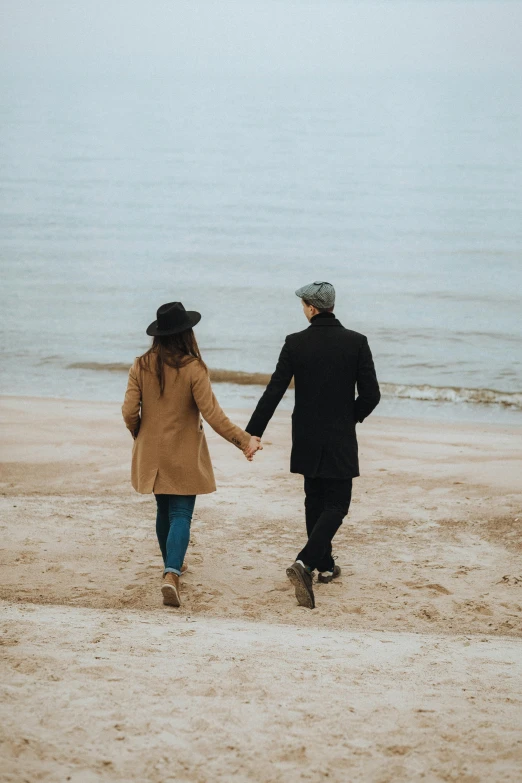 a man and woman walking on a beach holding hands, by Arabella Rankin, pexels contest winner, straw hat and overcoat, attractive girl, mittens, 1 2 9 7