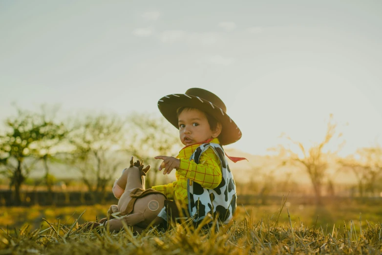 a baby in a cowboy outfit sitting in a field, pexels contest winner, in style of disney pixar, avatar image, sundown, woody from toy story