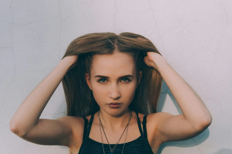 a beautiful young woman standing in front of a white wall, inspired by Elsa Bleda, pexels contest winner, photorealism, resembling a mix of grimes, hands in her hair, dark blonde hair, teenager girl