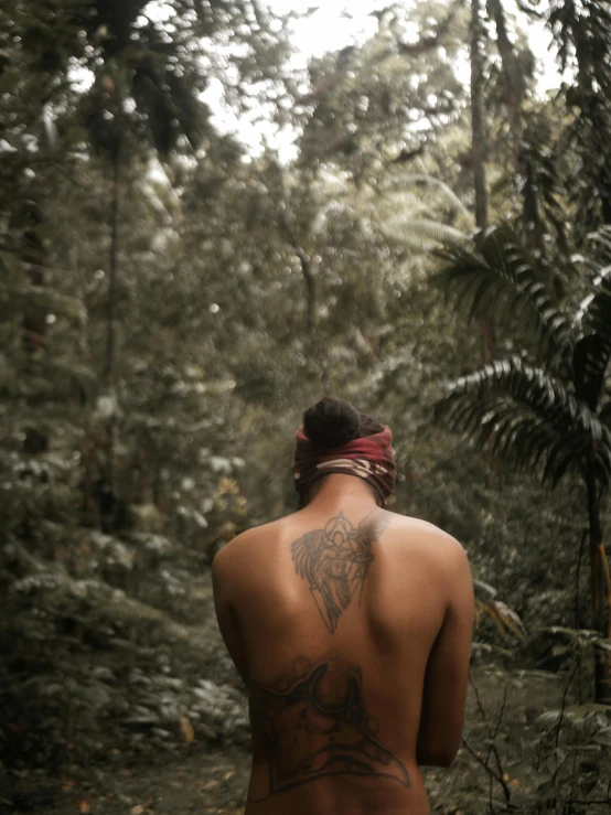 a man with a tattoo on his back walking in the woods, pexels contest winner, sumatraism, disrobed, tropics, low quality photo, looking out