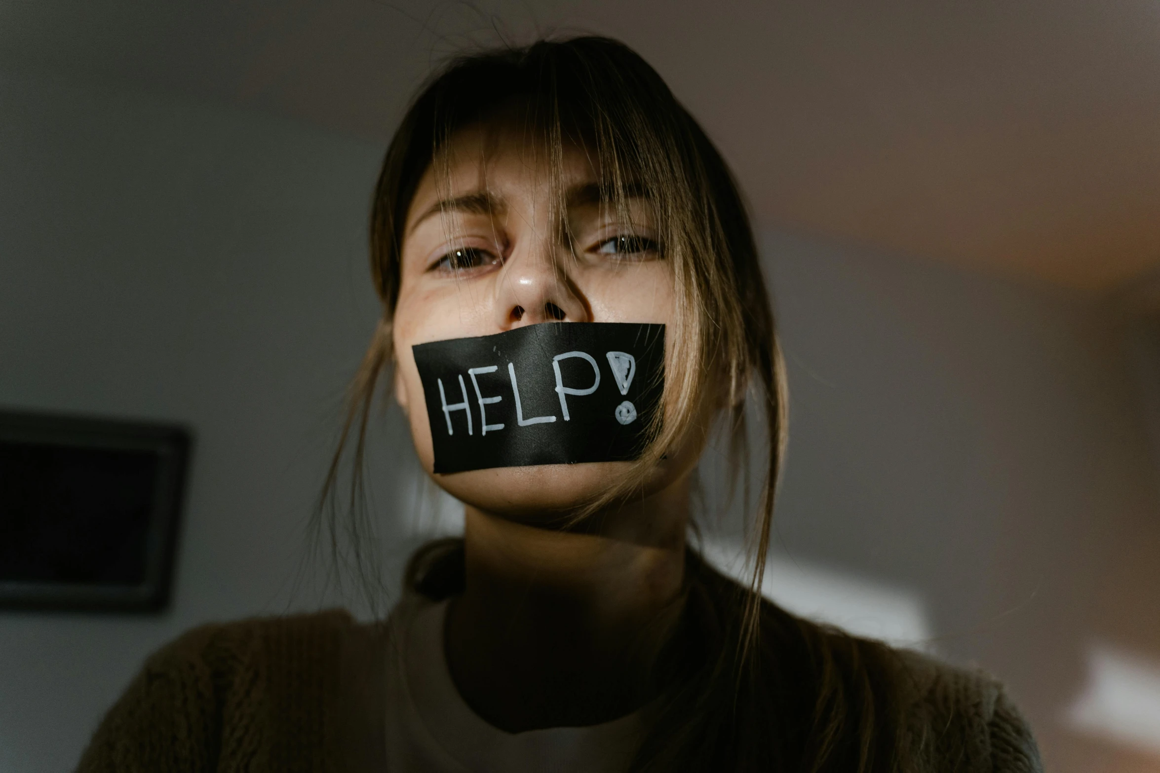 a woman with tape over her mouth saying help, a picture, trending on pexels, avatar image, 2263539546], cruelty, woman holding sign