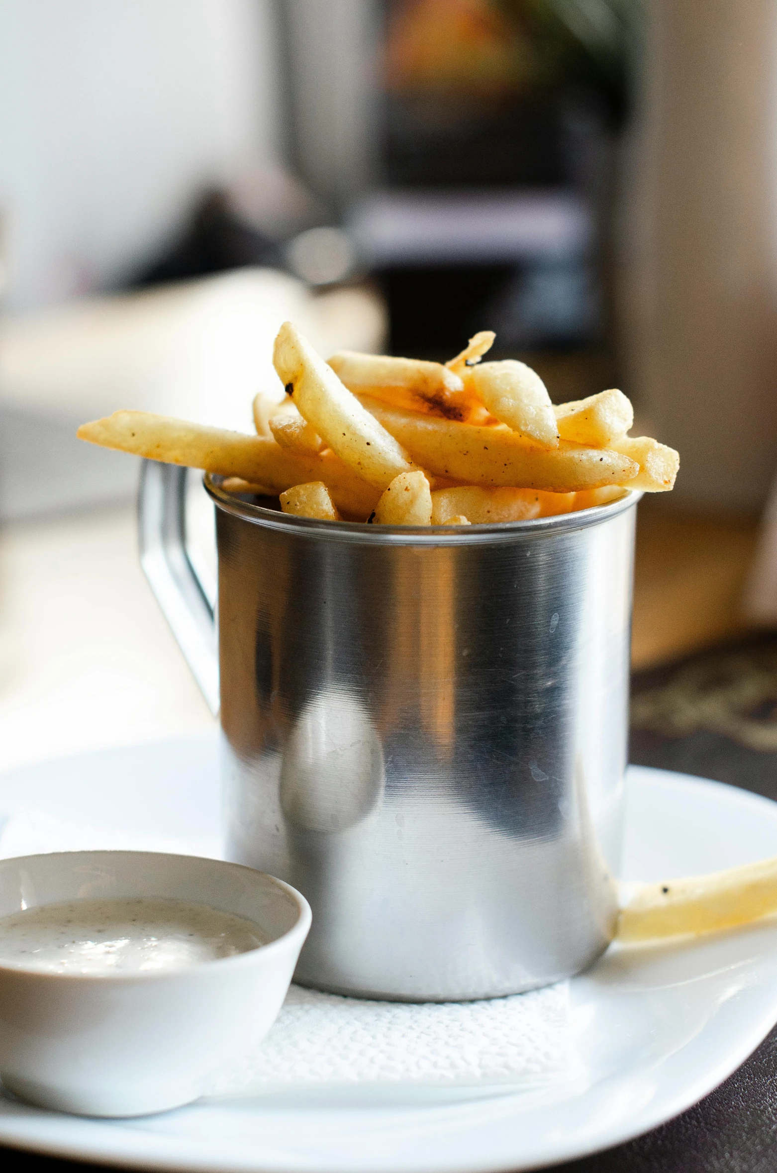 a white plate topped with french fries next to a cup of sauce, a still life, white and silver, melbourne, pot, exterior shot