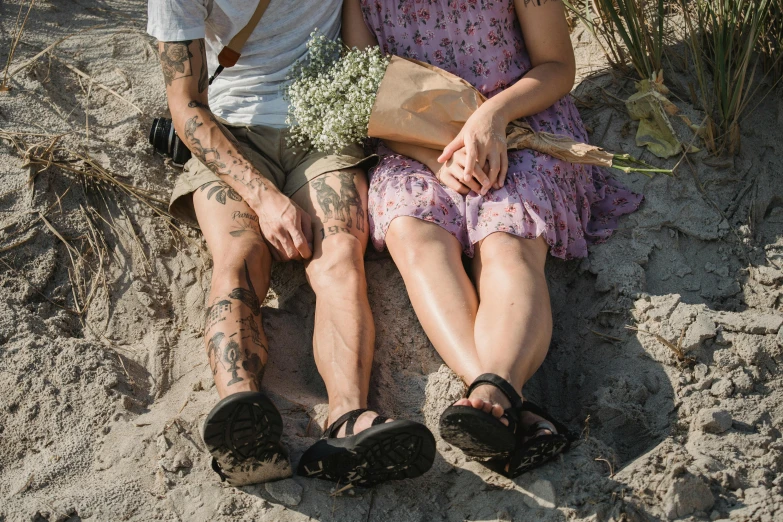 a man and a woman sitting in the sand, a tattoo, by Jessie Alexandra Dick, pexels contest winner, carrying flowers, detailed shot legs-up, photograph of a sleeve tattoo, cottagecore hippie