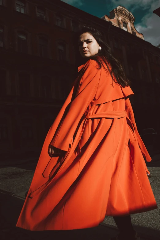 a woman in an orange coat walking down a street, an album cover, by Miroslava Sviridova, pexels contest winner, renaissance, marina abramovic, longcoat, portrait of alexandra daddario, fashion model