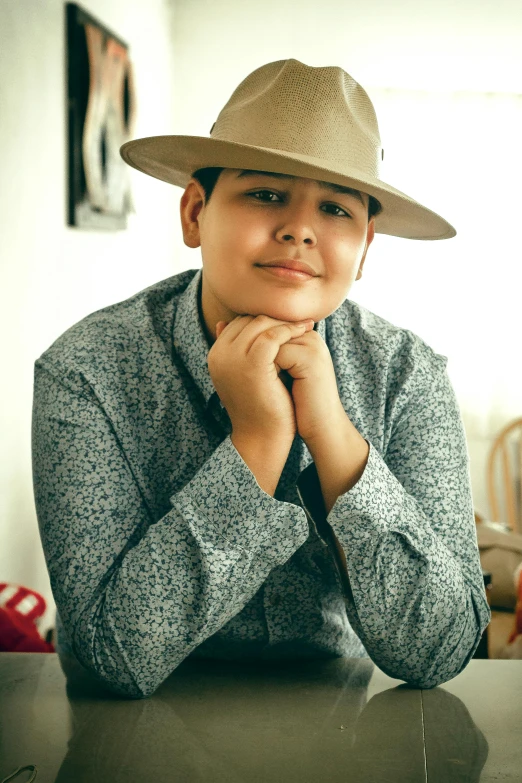 a man wearing a hat sitting at a table, androgynous person, alanis guillen, boy with neutral face, profile image