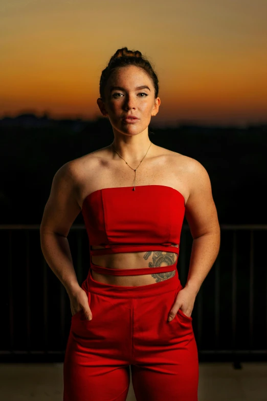 a woman in a red top and red pants, a portrait, by Winona Nelson, pexels contest winner, the body of ronda rousey, sun down, portrait photo of a backdrop, looking serious