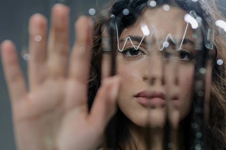 a woman holding her hands up in front of her face, a picture, by Adam Marczyński, pexels contest winner, electronics see through, made of glass, serious focussed look, photo of the beauty gal gadot