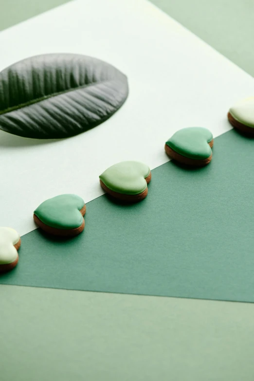 a green leaf laying on top of a piece of paper, cookies, several hearts, with celadon glaze, detailed product image