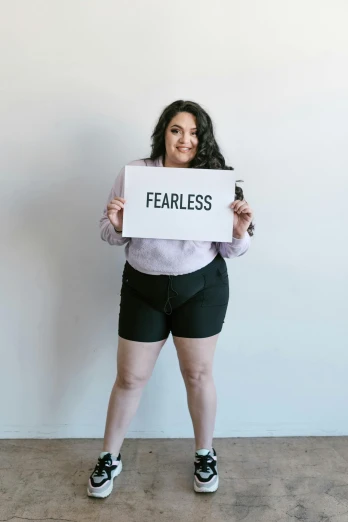 a woman holding a sign that says fearless, pexels contest winner, thick body, wearing shorts, promo image, rebecca sugar