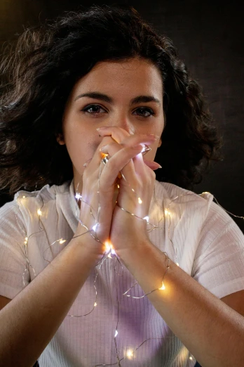 a woman sitting at a table with a glass of wine, string lights, hands on face, soft an diffuse lights, plain background