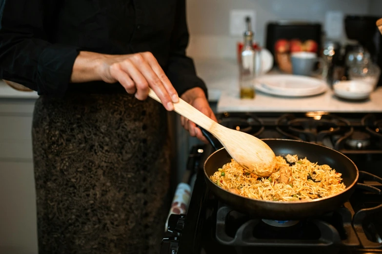 a woman cooking food in a frying pan on a stove, by Carey Morris, pexels contest winner, holding a wooden staff, rice, slightly golden, noelle stevenson
