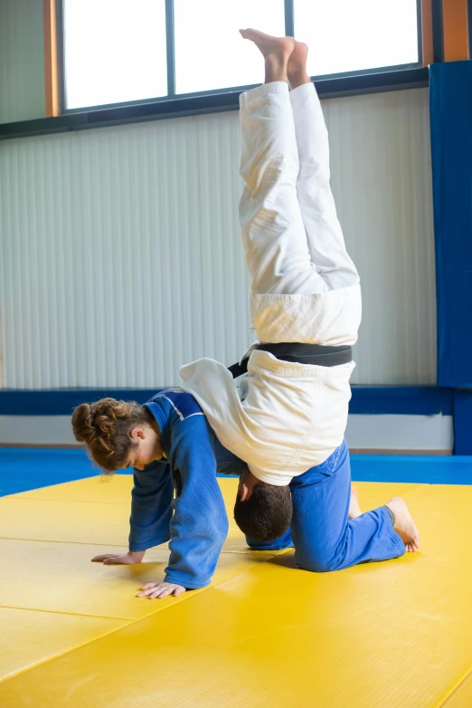 a person doing a handstand on a mat, wearing blue robe, action sports, wearing a tracksuit, white