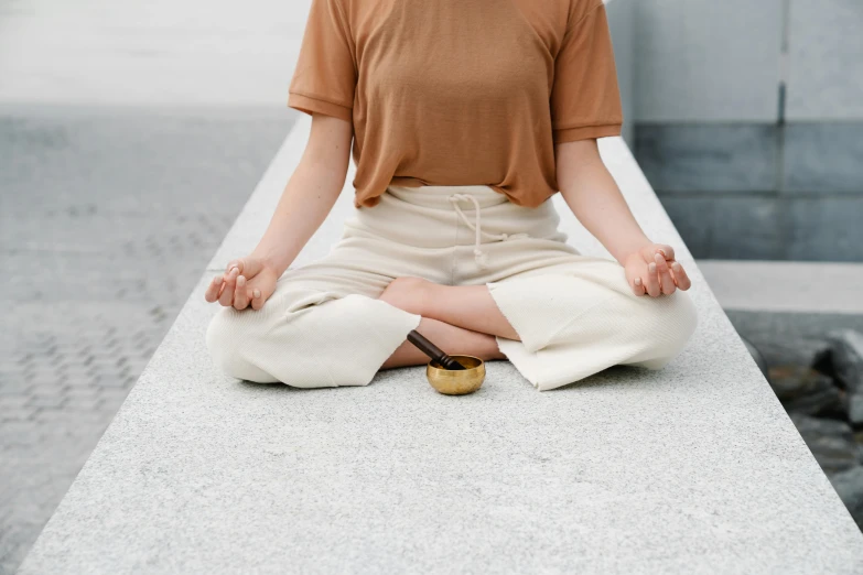 a woman sitting in a lotus position on a ledge, trending on pexels, minimalism, holding a golden bell, knees tucked in, brown, glazed