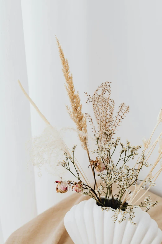 a close up of a vase with flowers in it, trending on unsplash, light and space, dry grass, in a white boho style studio, shades of gold display naturally, high quality product photo