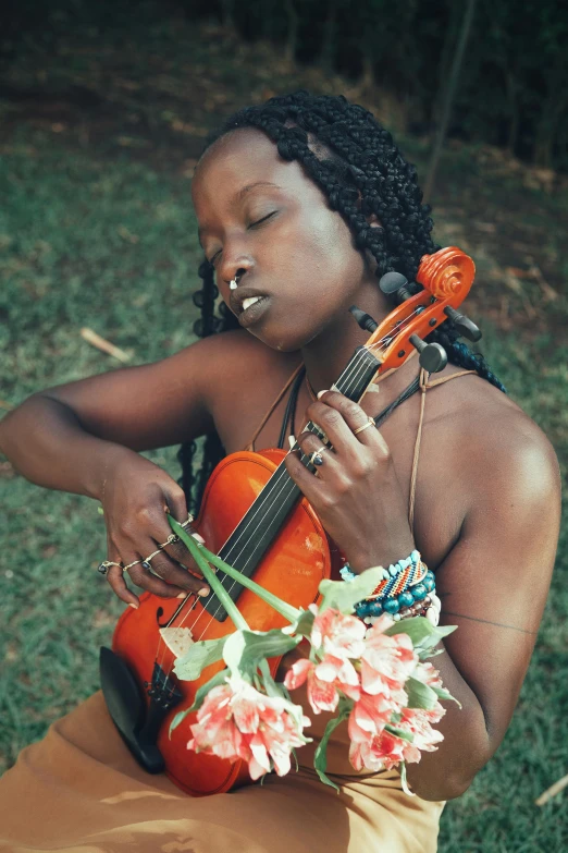 a woman sitting in the grass playing a violin, an album cover, by Ingrida Kadaka, pexels contest winner, holding flowers, african, sensuous, performing