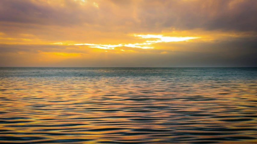 a large body of water under a cloudy sky, by Carey Morris, pexels contest winner, dappled golden sunset, ripples, tropical ocean, on a reflective gold plate