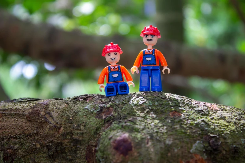 a couple of figurines sitting on top of a tree branch, a cartoon, inspired by Henry Woods, pexels contest winner, blippi, made of lego, standing in the forrest, miners