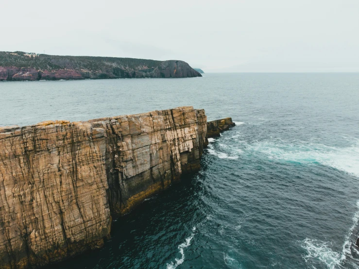 a man standing on top of a cliff next to the ocean, by Lee Loughridge, pexels contest winner, les nabis, highly detailed rock structures, whealan, where a large, high angle vertical