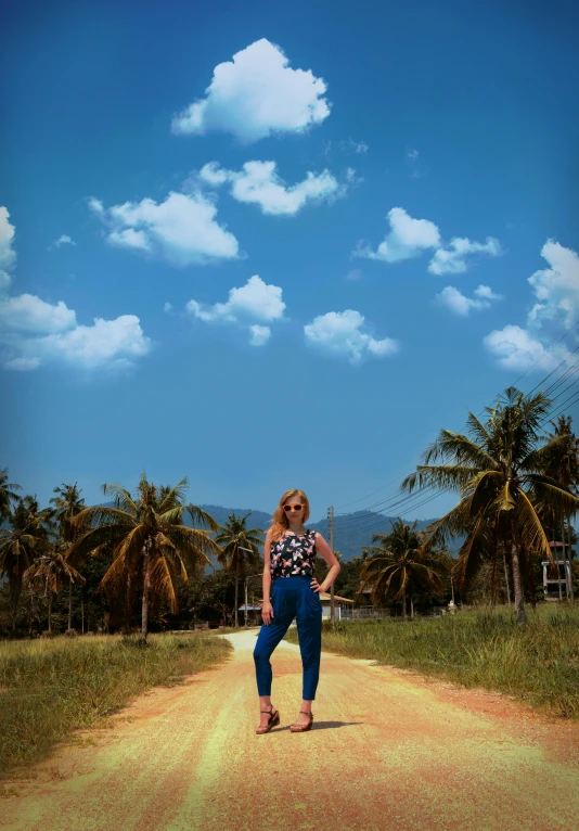 a woman standing in the middle of a dirt road, inspired by Max Buri, photorealism, 🌻🎹🎼, lomography photo effect, big blue sky, tropics