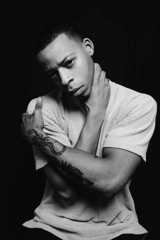 a black and white photo of a man with a tattoo on his arm, an album cover, inspired by Theo Constanté, black teenage boy, looking left, dr dre, androgynous male