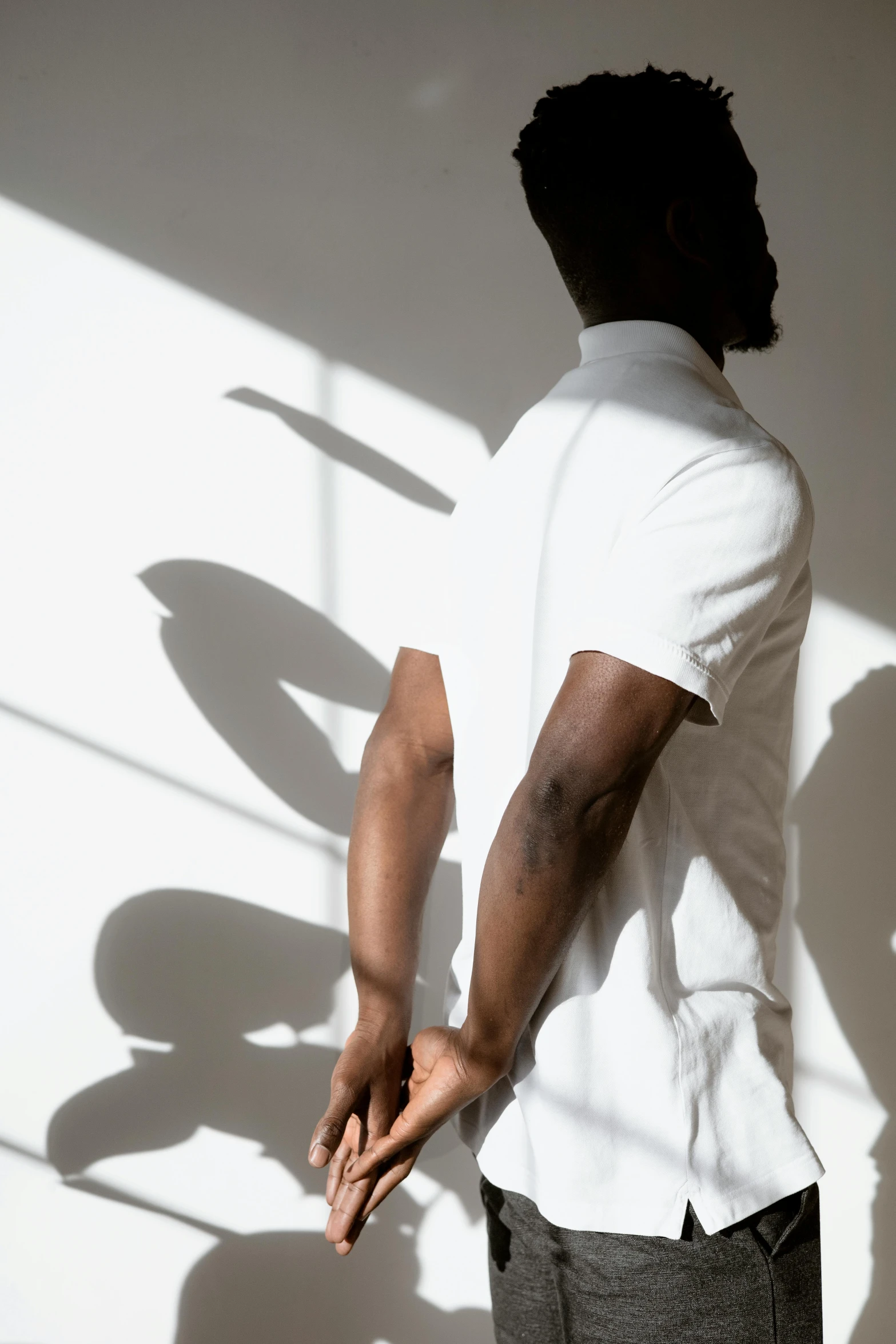 a man standing in front of a white wall, by Carey Morris, trending on unsplash, back light, wearing polo shirt, on a white table, consist of shadow