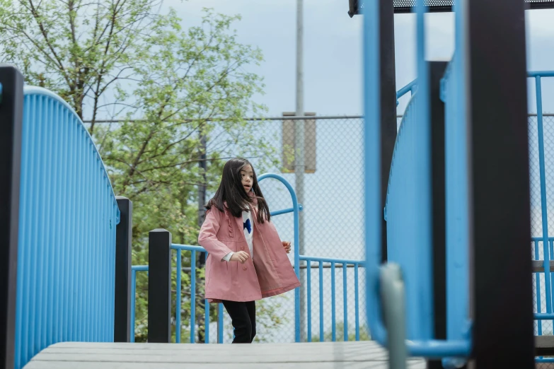 a woman in a pink coat walking down a set of stairs, unsplash, playground, blue slide park, standing astride a gate, black haired girl wearing hoodie