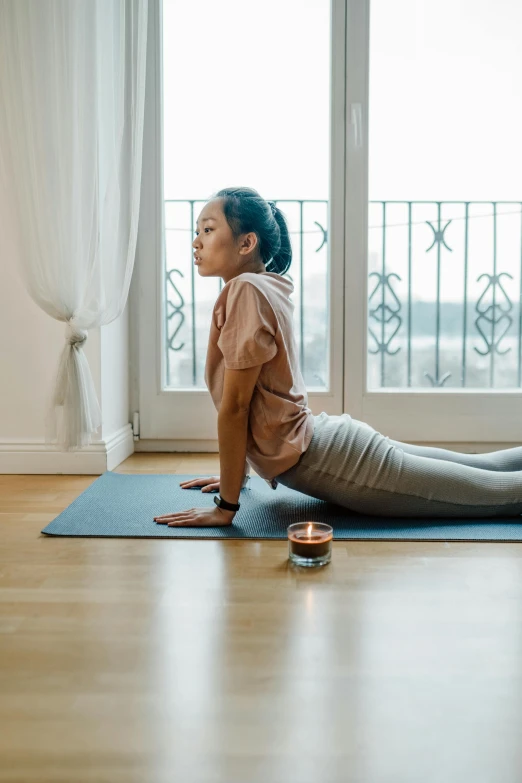 a woman sitting on a yoga mat in front of a window, pexels contest winner, renaissance, marjaryasana and bitilasana, malaysian, curved, glowing