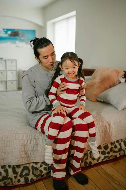 a man and a little girl sitting on a bed, inspired by Waldo Peirce, pexels contest winner, japanese collection product, stripey pants, crimson and ecru color scheme, nursing