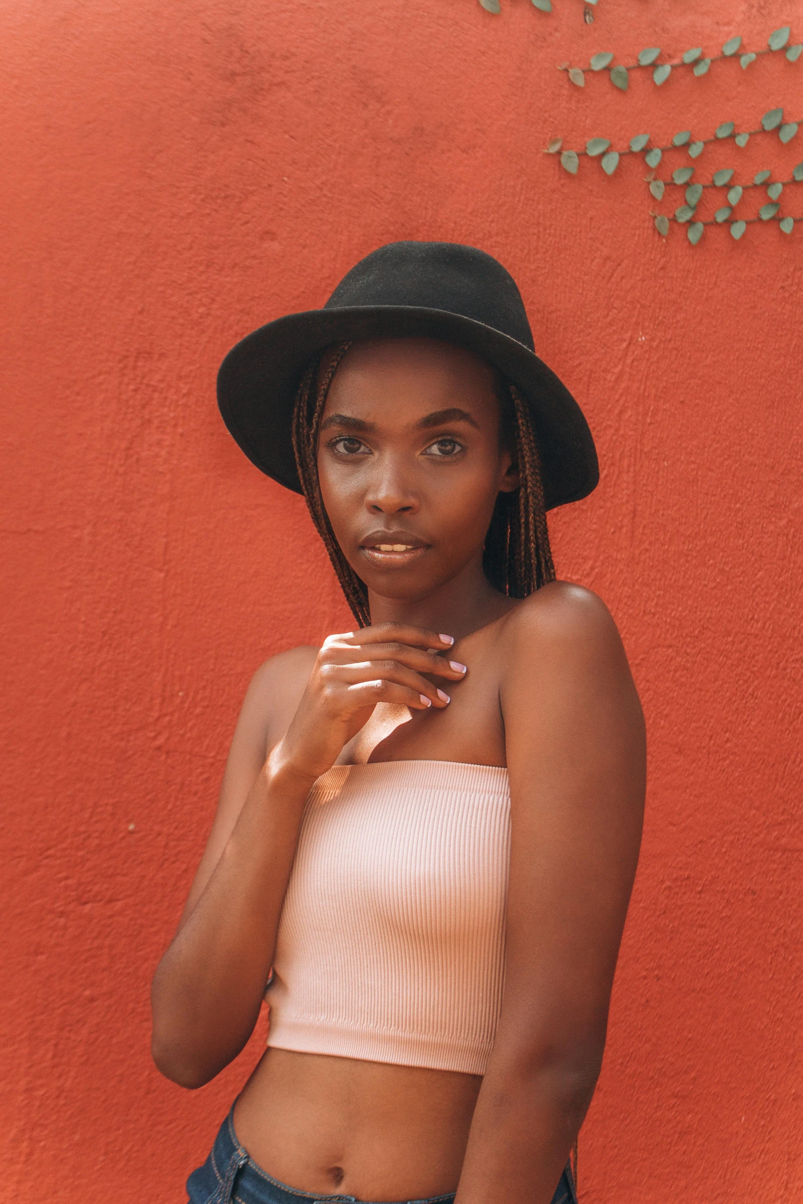 a woman standing in front of a red wall, by Arie Smit, pexels contest winner, wearing black dress and hat, brown skin. light makeup, black teenage girl, wearing a camisole