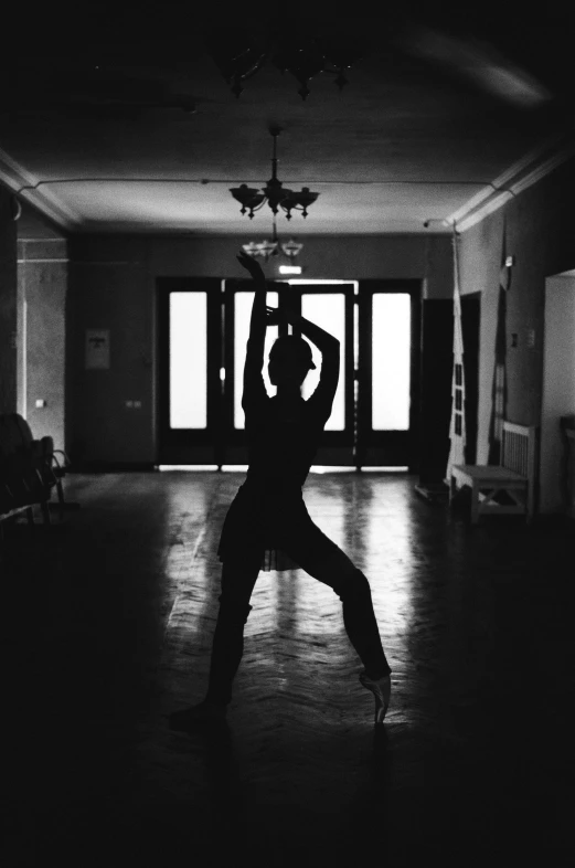 a black and white photo of a person doing a yoga pose, by Dimitre Manassiev Mehandjiysky, unsplash, arabesque, standing in a dimly lit room, palace dance, silhouette!!!, analog photo