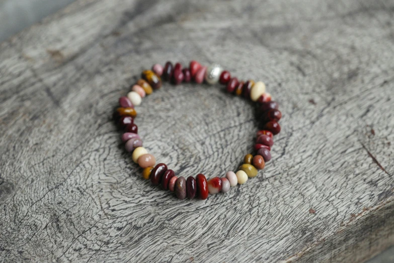 a close up of a bracelet on a wooden surface, by Nina Hamnett, instagram, dark oranges reds and yellows, pebbles, made of glazed, teenage girl