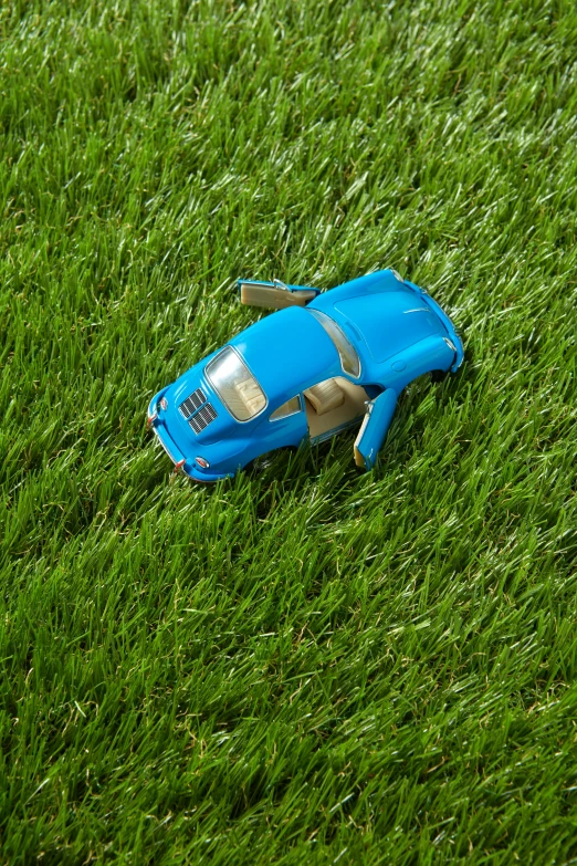 a toy car sitting on top of a lush green field, blue grass, fake grass, medium poly, top down angle