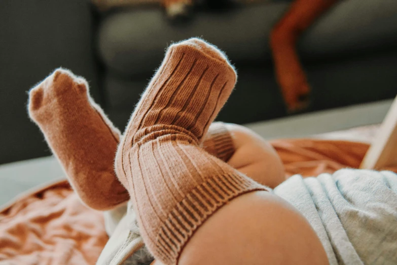 a close up of a person laying on a bed, trending on pexels, knee high socks, young child, brown, manuka